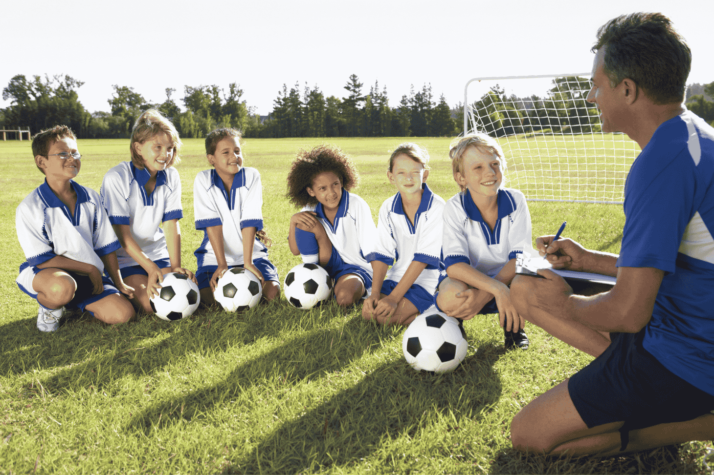 Jeunes footballeurs et leur entraîneur sur terrain foot avec ballons foot